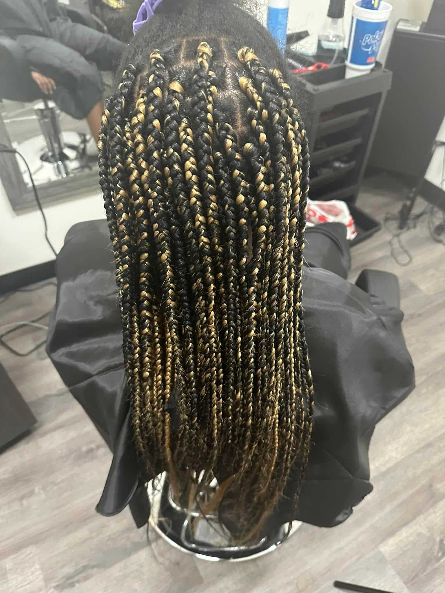 Person with long, intricate black and blonde braids sitting in a salon chair.