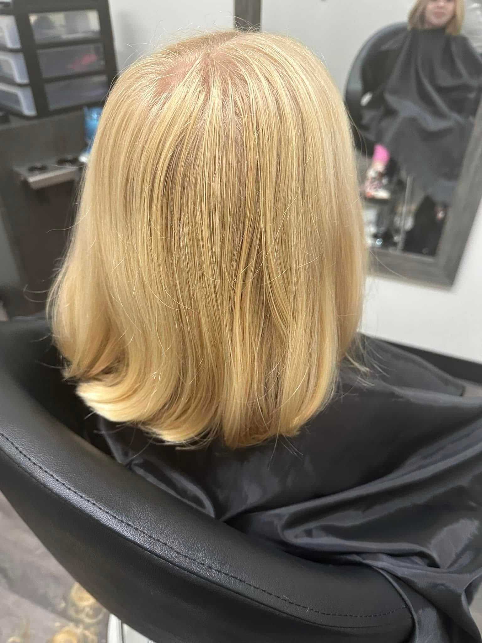 Back view of a woman getting a blonde bob haircut in a salon.
